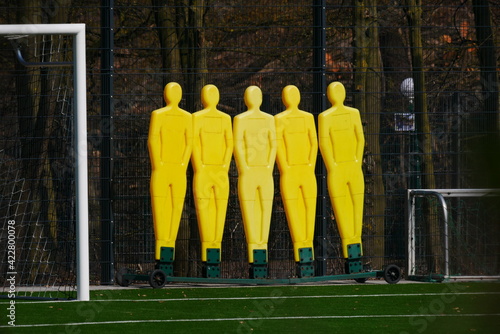 Fotografija yellow training free kick dummies next to the playing field and soccer goal