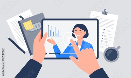 A workplace with coffee, notebook, papers, and tablet. A hand is holding a tablet with a video player. Vector flat illustration.