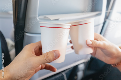 Happy man and a woman clink paper cups in the interior of an airplane during a vacation flight. Catering and wine tasting