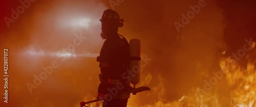 Dramatic silhouette of American firefighter in full gear exploring the huge fire zone. Shot with 2x anamorphic lens  photo