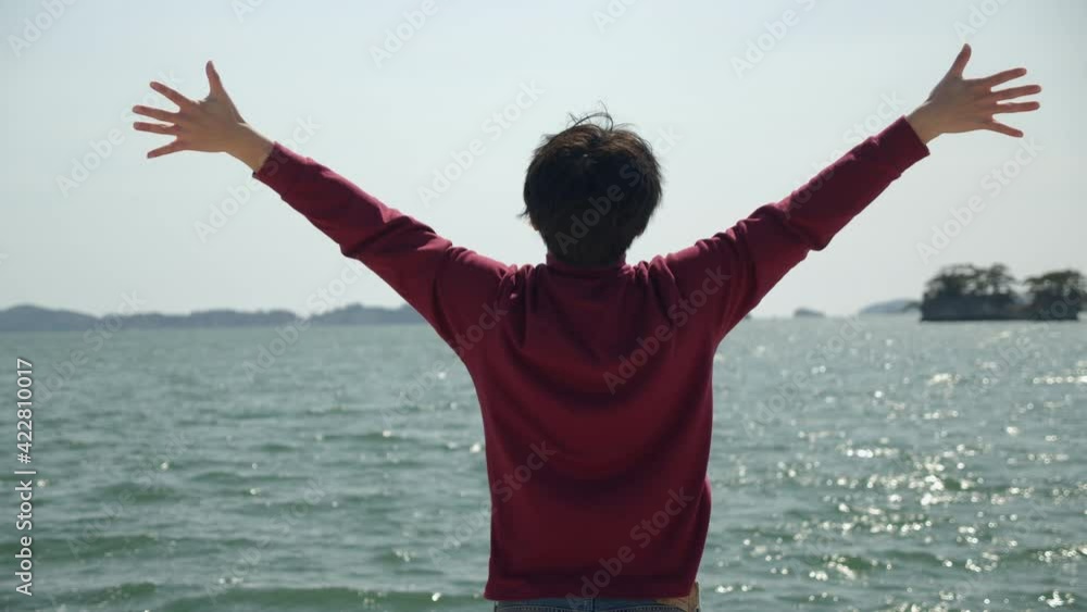 Excited young man extends his arms and full of vigor embraces the ocean. Morning stretch by the ocean, camera panning. Excited young man extends his arms and full of vigor embraces the ocean. Morning stretch by the ocean, camera panning.
