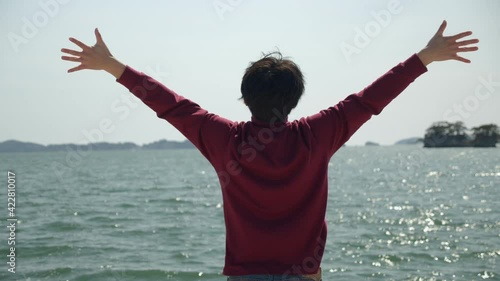 Excited young man extends his arms and full of vigor embraces the ocean. Morning stretch by the ocean, camera panning.