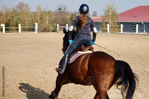 Young horsewoman riding on brown horse in paddok outdoors, copy space. Equestrian sport.