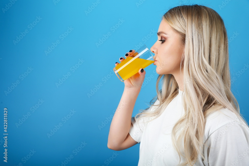 young woman is drinking yellow soda water on blue background. girl holding a glass of lemonade young woman is drinking yellow soda water on blue background. girl holding a glass of lemonade