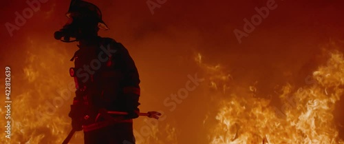 Dramatic shot of American firefighter in full gear walking through smoke away from fire. Shot with 2x anamorphic lens  photo