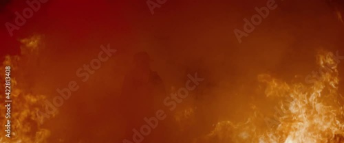 Dramatic shot of American firefighter in full gear walking into smoke and huge fire. Shot with 2x anamorphic lens  photo