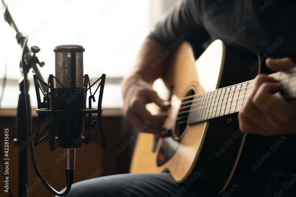Fototapeta premium Man playing acoustic guitar and recording with a microphone in a room. Home studio