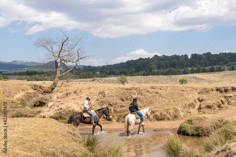 Dos jóvenes con sus caballos están saliendo de un arroyo. 