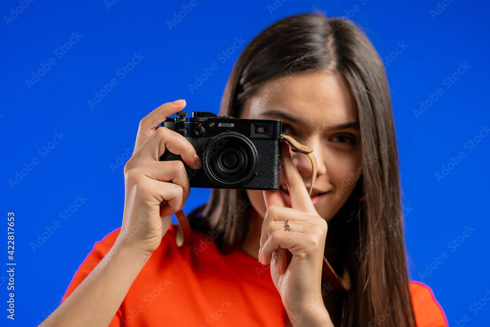 Young pretty woman takes pictures with DSLR camera over blue background in studio. Girl smiling as photographer. Young pretty woman takes pictures with DSLR camera over blue background in studio. Girl smiling as photographer.