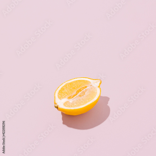 Lemon half on a pale pink background. Sunlit vintage yellow summer fruit with shadow. Retro beach food aesthetic layout.