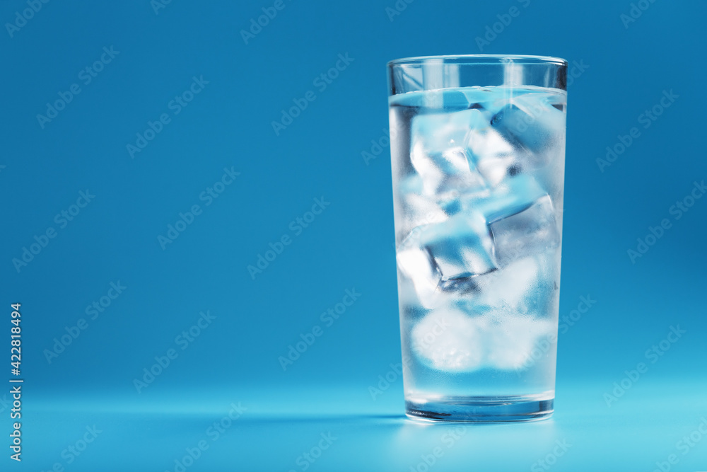 Ice cubes in a glass with crystal clear water on a blue background. Ice cubes in a glass with crystal clear water on a blue background.