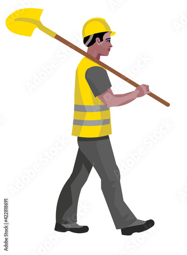 A dark-skinned construction worker walks with a shovel on his shoulder in a work vest and hard hat