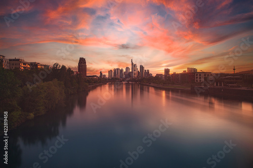 Frankfurt am Main city in the setting sun with reflection in the river and floating clouds in the sky.