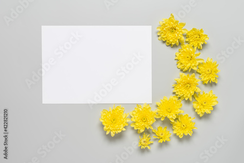 Blank white paper card mockup with yellow flowers on gray background. Top view, flat lay.