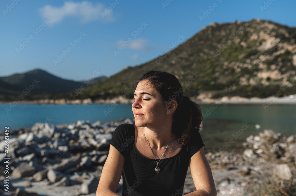 Woman at the sea with cheerful face resting on the fence enjoying the sun with closed eyes.