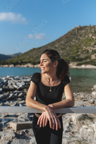 Vertical  portrait woman at the sea with cheerful happy face resting on the fence enjoying the sun with closed eyes. © Pintau Studio