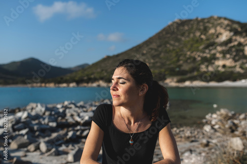 Woman at the sea with cheerful face resting on the fence enjoying the sun with closed eyes. © Pintau Studio