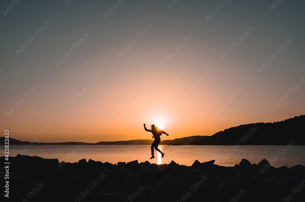 Silhouette of traveler on seashore jumping at the beach during sunset.