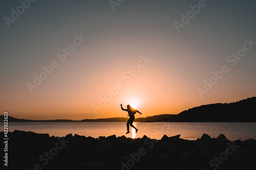 Silhouette of traveler on seashore jumping at the beach during sunset.