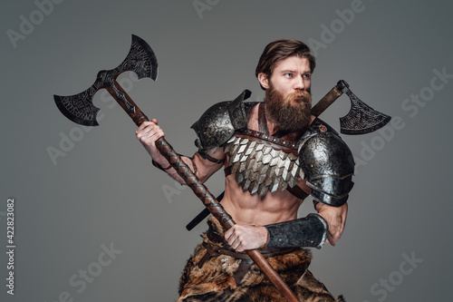 Savage nordic barbarian with an axe posing in gray background