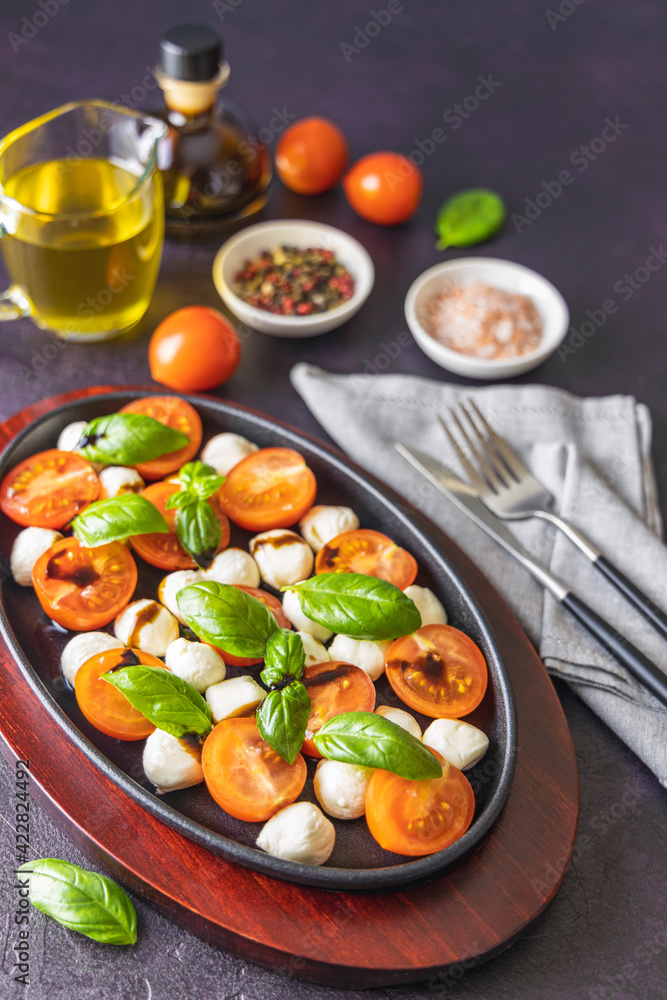 Caprese salad with cherry tomatoes, mozzarella and basil in oval black plate Caprese salad with cherry tomatoes, mozzarella and basil in oval black plate