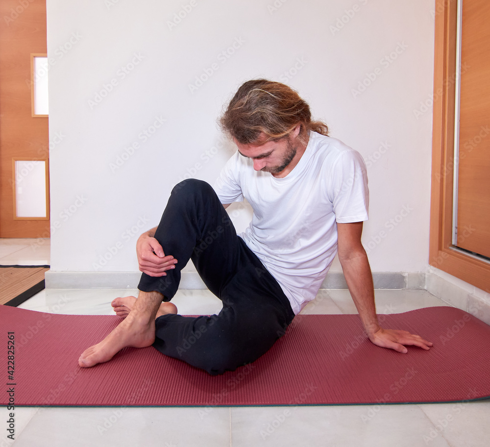 Spanish bearded young male in sportswear stretching on the yoga mat at home