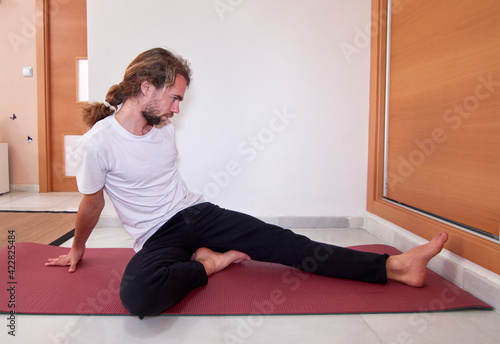 A side view of a Spanish bearded young male in sportswear practicing yoga on the yoga mat at home