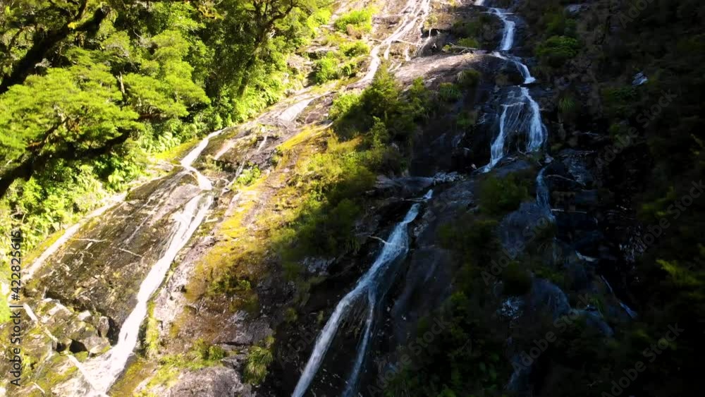 Small Waterfall Cascading Down Mountainside - tilt up wide shot Small Waterfall Cascading Down Mountainside - tilt up wide shot
