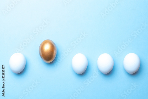 Easter holiday. Golden, white colour egg on pastel blue background in Happy Easter decoration. Spring holiday top view with copy space.