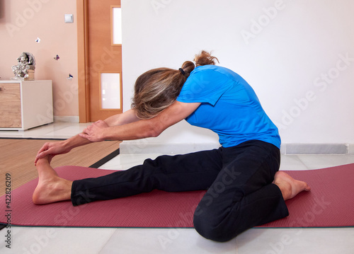 A side view of a Spanish bearded young male in sportswear stretching on the yoga mat at home