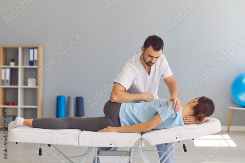 Confident man doctor chiropractor or osteopath fixing womans back and legs joints photo