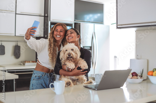 Two friends taking a selfie with the smart phone while having coffee together in the kitchen at home photo