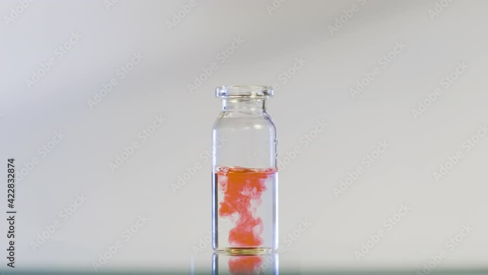 A red liquid is dropped into a flask with a clear liquid. The flask rotates in the center and the red substance slowly dissolves. Chemical quality test. A red liquid is dropped into a flask with a clear liquid. The flask rotates in the center and the red substance slowly dissolves. Chemical quality test.