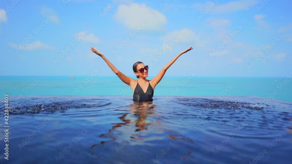 Happy asian woman spaying water in infinity swimming pool on sunny tropical day. Luxury vacation concept, full frame Happy asian woman spaying water in infinity swimming pool on sunny tropical day. Luxury vacation concept, full frame