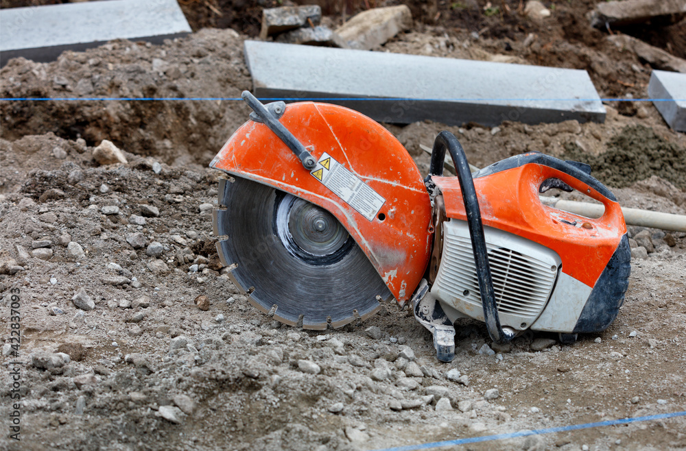 Petrol saw with diamond wheel on construction site gravel in front of concrete parapets.