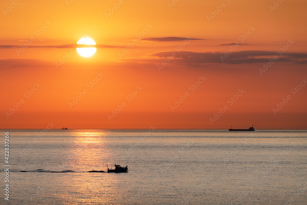 Sunset in the ocean with large sun dusk in orange sky and ships and boats silhouettes. Sea sunrise background. Landscape photography Sunset in the ocean with large sun dusk in orange sky and ships and boats silhouettes. Sea sunrise background. Landscape photography