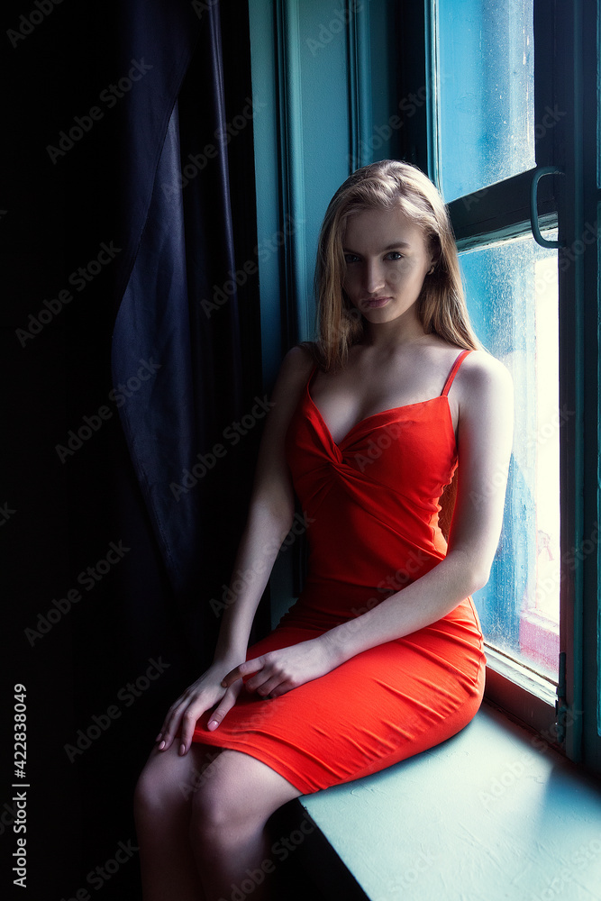 beautiful girl in a red dress is sitting on the windowsill