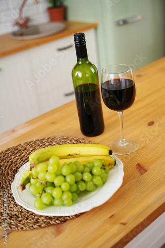 Close up of bottle and glass of red wine with berries and fruits on plate. Preparation on table for dating in kitchen.