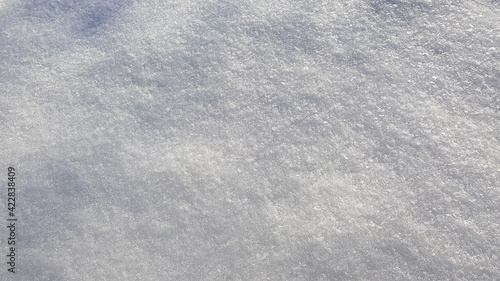 Winter background with snow close-up, top view. On a sunny day outdoors. Pure and shiny snow, with highlights and shadows. Loose gray snow, natural texture. Copy space, no people. 