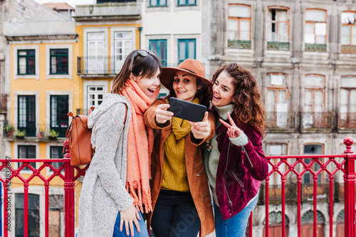 three women sightseeing Porto views and taking picture with mobile phone. Travel and friendship concept