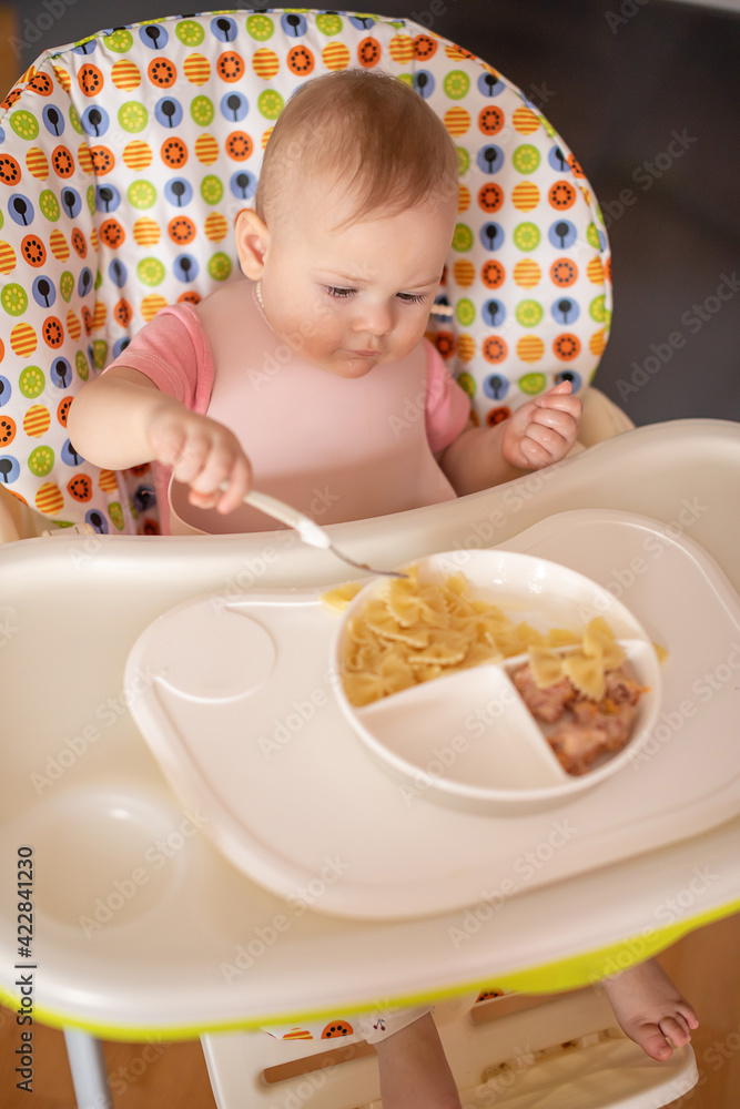 One year old girl having balanced meal in baby eating chair, healthy balanced nutrition for child One year old girl having balanced meal in baby eating chair, healthy balanced nutrition for child