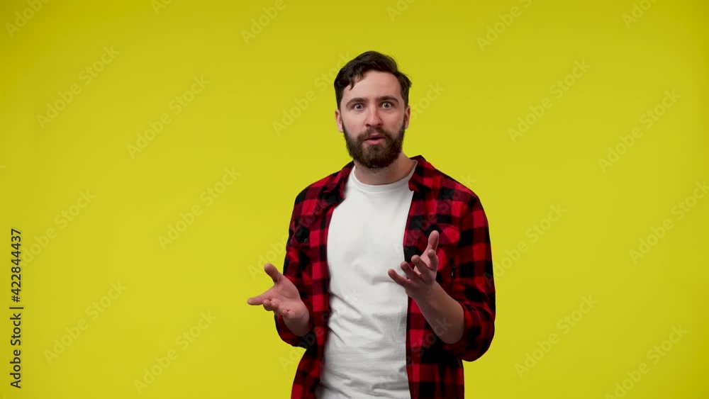 Surprised shocked bearded young man, throws out his arms, says wow with an impressed face, grabs his temples. A man in the studio on a yellow background. Close up. Slow motion ready 59.97fps. Surprised shocked bearded young man, throws out his arms, says wow with an impressed face, grabs his temples. A man in the studio on a yellow background. Close up. Slow motion ready 59.97fps.