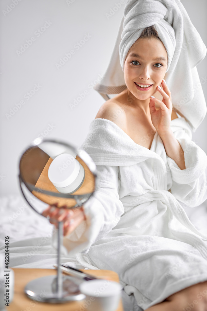 pretty woman in white towel chilling in bedroom and looking at small mirror, going to do beauty procedures