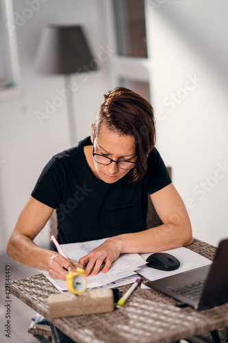 Serious looking mature woman with laptop and paperwork,analyzing bills