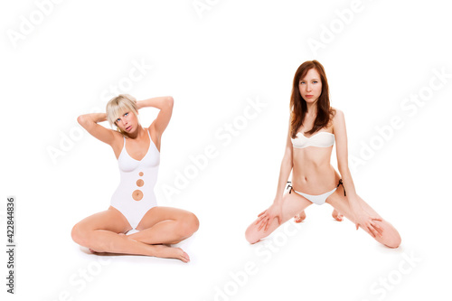 Portraits of two beautiful young women wearing white bikinis and swimsuits, isolated on white studio background