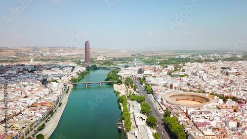 Drone flying above the famous Guadalquivir River in the center of Seville City, At right the Bull Ring and Theatre of Seville. In front Triana Bridge. Drone forward, beautiful perspective of the city.