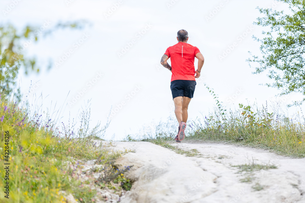 Sporty bearded man running on the path at hillside
