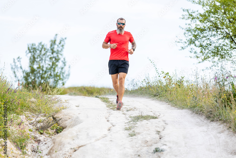 Sporty bearded man running on the path at hillside Sporty bearded man running on the path at hillside