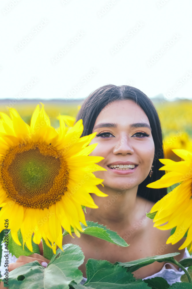 Beautiful brunette woman in a white top on the field with sunflowers. Yellow sunflowers. Close plan. Beautiful brunette woman in a white top on the field with sunflowers. Yellow sunflowers. Close plan.