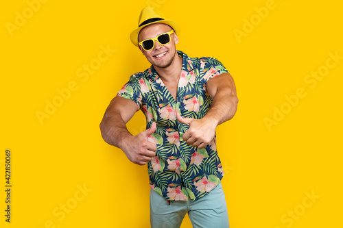 Young sportve man on vacation wearing floral summer shirt over yellow background success sign doing positive gesture with hand, thumbs up smiling and happy. Cheerful expression and winner